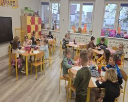 Dzieci uśmiechnięte tańczą z misiami oraz siedzą przy stolikach i kolorują obrazki misiów