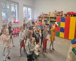 Dzieci uśmiechnięte tańczą z misiami oraz siedzą przy stolikach i kolorują obrazki misiów