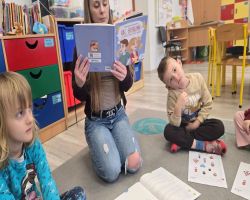 Dzieci siedzą na dywanie w kole i słuchają opowiadania.