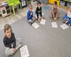 Dzieci siedzą na dywanie w kole i słuchają opowiadania.