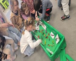 Dzieci świętują Dzień Dinozaura. Siedzą razem na dywanie i tworzą makietę.