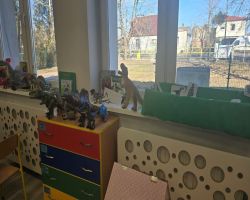 Dzieci świętują Dzień Dinozaura. Siedzą razem na dywanie i tworzą makietę.