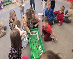 Dzieci świętują Dzień Dinozaura. Siedzą razem na dywanie i tworzą makietę.