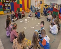 Dzieci świętują Dzień Dinozaura. Siedzą razem na dywanie i tworzą makietę.