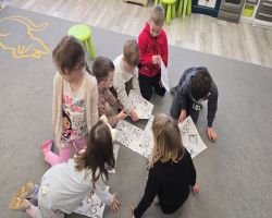 Dzieci siedzą na dywanie i prezentują swoje ulubione książki.