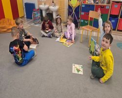 Dzieci siedzą na dywanie i prezentują swoje ulubione książki.