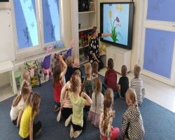 Przedszkolaki tworzą kreatywne prace plastyczne przy stolikach, a następnie sadzą drzewa w ogrodzie.