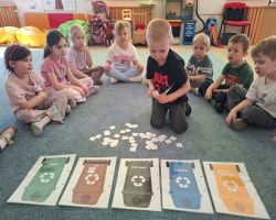 Przedszkolaki tworzą kreatywne prace plastyczne przy stolikach, a następnie sadzą drzewa w ogrodzie.